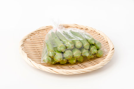 fresh Okra in plastic bag on bamboo sieve on white backgroundの写真素材