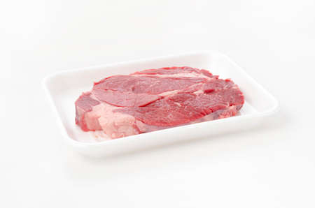 Fresh raw beef steak on foam tray on white background