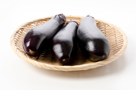 fresh black eggplant on bamboo sieve on white backgroundの写真素材