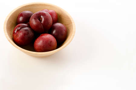 Japanese plum (Prunus salicina) in a round wooden bowl on white backgroundの写真素材