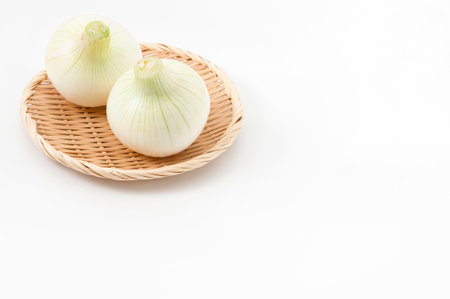Seasonal onions on a bamboo sieve on white backgroundの写真素材