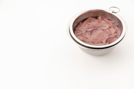 Draining blood from pork liver in a stainless steel bowl filled with water on white background