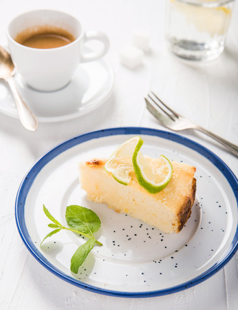 Cheesecake with ricotta cheese on a beautiful plate, vintage fork, a cup of aromatic espresso and water with lemon. Italian food. Sweets. White vintage background.の写真素材