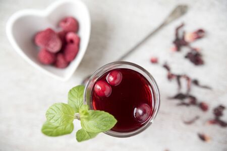 Red hibiscus tea in a beautiful cup, raspberries in a heart-shaped plate. Copy spaceの写真素材