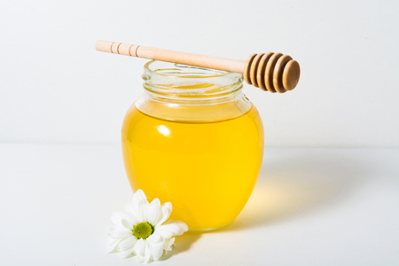 Light honey in the jar with spoon and flower on the white backgroundの写真素材