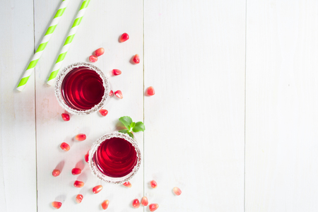 Red pomegranate  beverage in two glasses with sugar decoration on white wooden background with copy space, top viewの写真素材