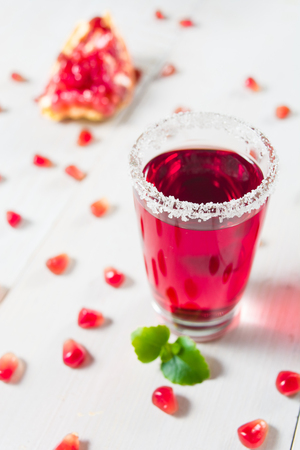 Pomegranate drink in glass with sugar decoration on white wooden background, vertical shotの写真素材