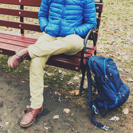 Young traveler or student sitting on bench and waiting in autumn or spring park with backpackの写真素材