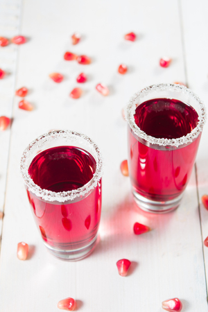 Two red beverages of pomegranate with sugar decoration on white wooden background, vertical shotの写真素材