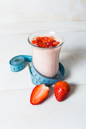 Strawberry yogurt smoothie with measure tape on white wooden background. Vertical shotの写真素材