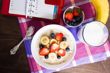 Healthy breakfast with oatmeal, banana, strawberry, blueberry and milk with planning concept on the wooden table, top viewの写真素材