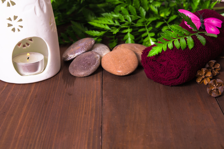 Candle in aroma lamp, stones and towel decorated with fern and paper butterfly on the wooden backgroundの写真素材