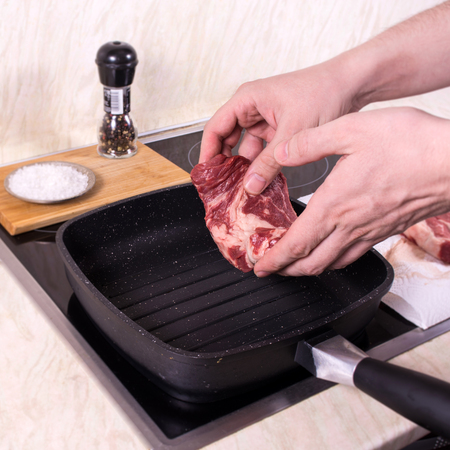 Young man put one piece of steak on hot grill pan with spices on the backgroundの写真素材
