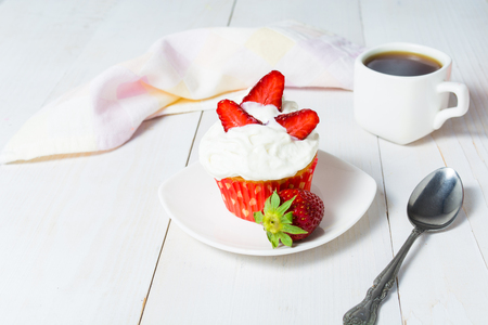 Strawberry cupcake with whipped cream and cup of coffee on white wooden table for breakfastの写真素材
