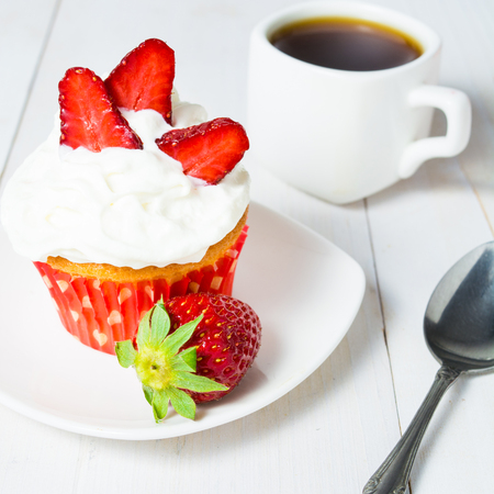 Strawberry cupcake with whipped cream and cup of coffee on white wooden tableの写真素材