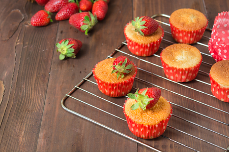 Muffins decorated with strawberry on baking pan over brown wooden table with copy spaceの写真素材