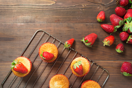Muffins decorated with strawberry on baking pan over brown wooden table with copy space, top viewの写真素材