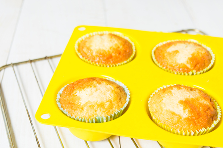 Muffins a moment ago from baking oven on baking pan in yellow silicon form over white wooden tableの写真素材