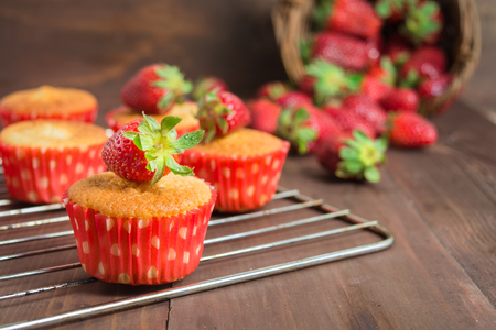 Muffins decorated with strawberry on baking pan over brown wooden table with copy spaceの写真素材