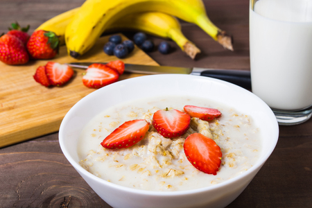 Ingredients (banana, strawberry, blueberry, milk) closeup for oatmeal on wooden boardの写真素材