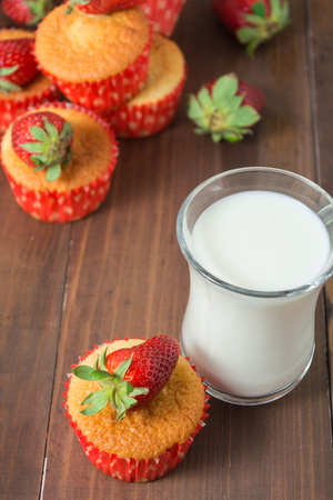 Muffins decorated with strawberry and glass of milk for breakfast over brown wooden tableの写真素材