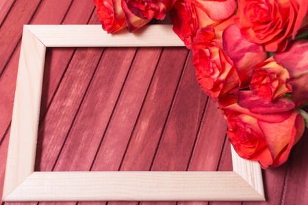 Wooden frame with bouquet of red roses on the red wooden table. Copy spaceの写真素材