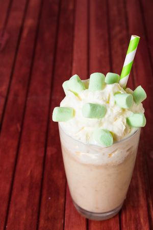 Banana milshake with marshmallow and whipped cream on the rad wooden backgroundの写真素材