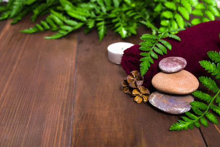 Spa still life with candle, stones and towel decorated fresh green fern on the wooden backgroundの写真素材