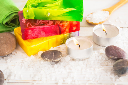 Spa still life with salt, stone and three pieces of soap with aroma lamp on the white wooden table with copy spaceの写真素材