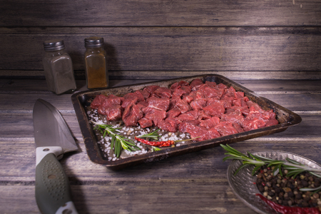Raw meat with salt, pepper and rosemary on the baking pan on the wooden tableの写真素材