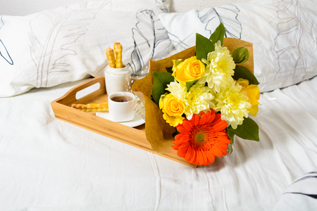 Tray with coffee, snack and bouquet of flowers over white bedclothesの写真素材
