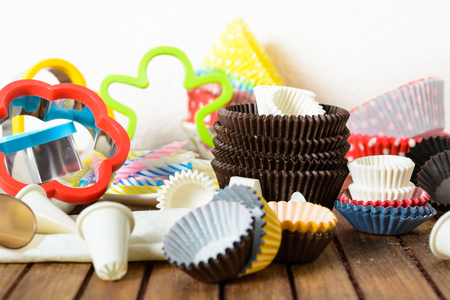 Different baking accessories for cupcake, muffins and cookies over brown wooden table and white backgroundの写真素材