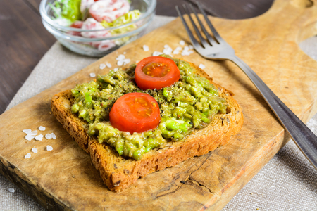 Avocado toast with whole wheat bread and vegetable salad on wooden tableの写真素材