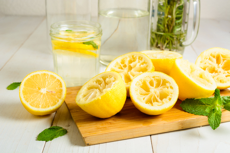 Squeezed lemons on board, mint and ready lemonade over white wooden backgroundの写真素材