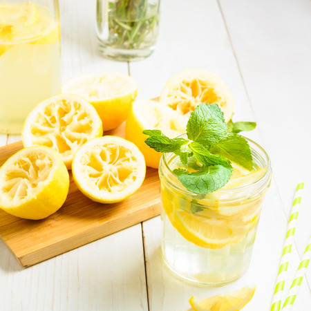 Lemonade with mint and squeezed lemons on board and two straw over white wooden background, square shotの写真素材