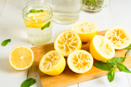 Squeezed lemons on board, mint and ready lemonade over white wooden backgroundの写真素材