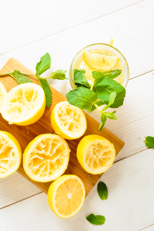 Lemonade with mint and squeezed lemons on board over white wooden background, top view, vertical shotの写真素材