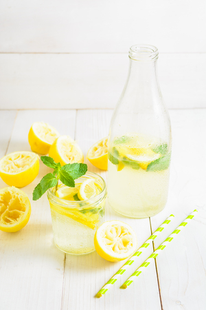Bottle of lemonade and lemonade in jar decorated with mint and two straw on white wooden background, vertical shotの写真素材