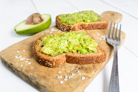 Homemade healthy avocado toast on wholegrain bread on board over white wooden backgroundの写真素材
