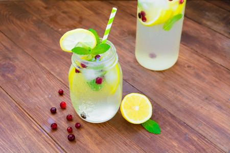 Jug with detox water with lemons, mint, ice and cranberry on brown wooden tableの写真素材