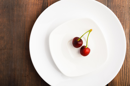 Red sweet cherry on two white plates over brown wooden table with top viewの写真素材