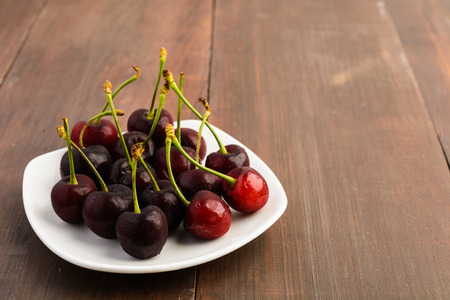 Many healthy cherries on white plate over brown wooden backgroundの写真素材