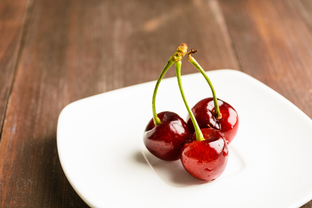 Three cherry on white plate on brown wooden backgroundの写真素材
