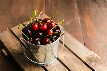 A bucket full of cherry over brown wooden background with copy spaceの写真素材