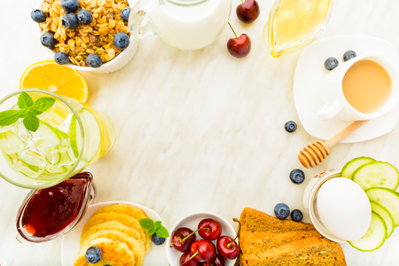Food frame of healthy breakfast with detox water, granola, coffee, berries, pancakes, egg and bread on light background with copy spaceの写真素材