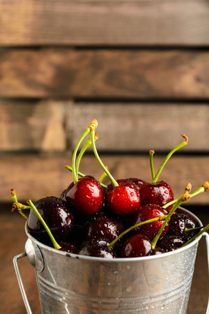 A bucket full of cherry over brown wooden background with copy space, vertical shotの写真素材