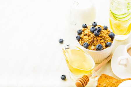 Muesli with honey, milk and blueberry like breakfast with detox water, coffee, bread with copy space on white backgroundの写真素材