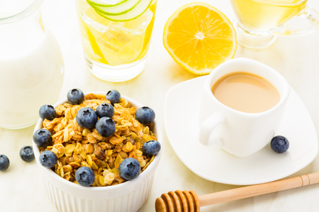 Breakfast with detox fresh water, granola, honey, coffee and milk on white table, horizontal shotの写真素材
