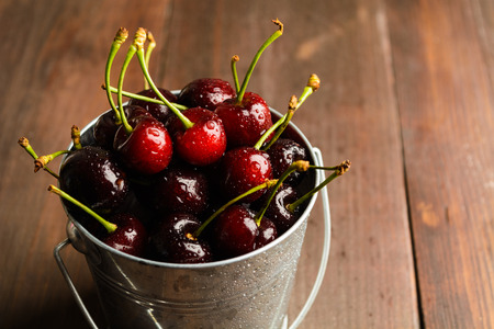 Closeup bucket full of cherry over brown wooden background with copy spaceの写真素材