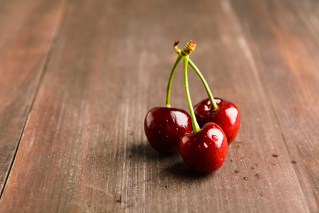 Three cherry with drop of water on brown wooden table with copy spaceの写真素材